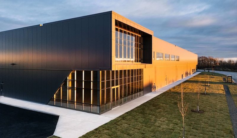 Le 8100, rue Armand-Viau Nord au crépuscule : un bâtiment industriel neuf au revêtement noir, sa façade vitrée allumée