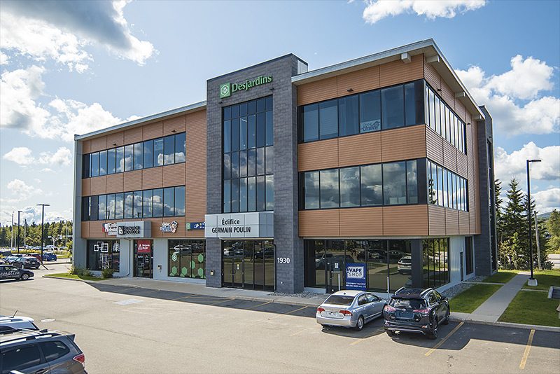 Le Carrefour de la Bravoure, un immeuble de bureaux de trois étages en brique et en panneaux gris, ciel bleu