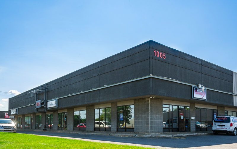 Le Carrefour du Commerce 1005, un bâtiment commercial noir à un étage, entrée vitrée et voitures devant