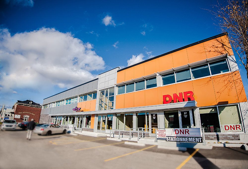 Le 55-57, rue Marie-de-l'Incarnation à Québec : un immeuble commercial de deux étages aux panneaux orange, ciel bleu, stationnement devant
